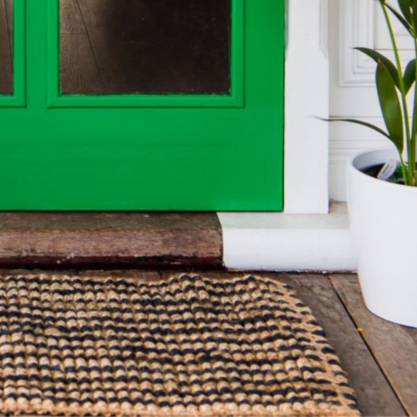 Handcrafted striped Caravan striped jute rug in a small size, placed at a green front door on wooden decking.
