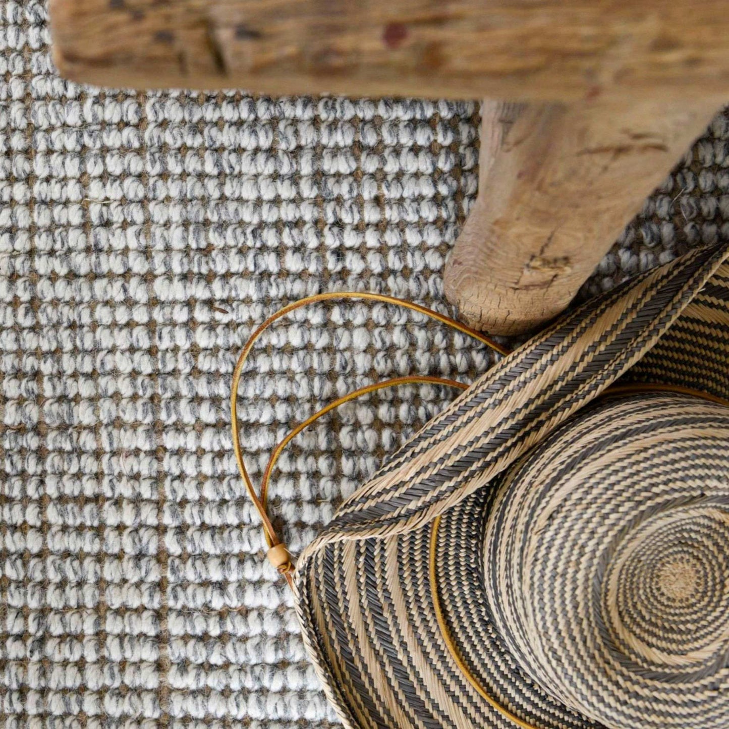 Close-up of the carter handcrafted, grey and white heathered wool and jute bouclé rug under a wooden bed frame.