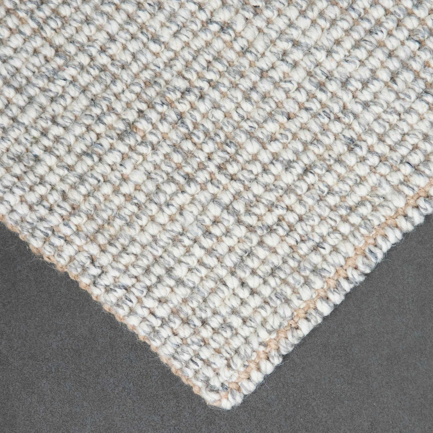 Close-up of Carter handcrafted grey white heathered wool and jute bouclé rug on slate background.