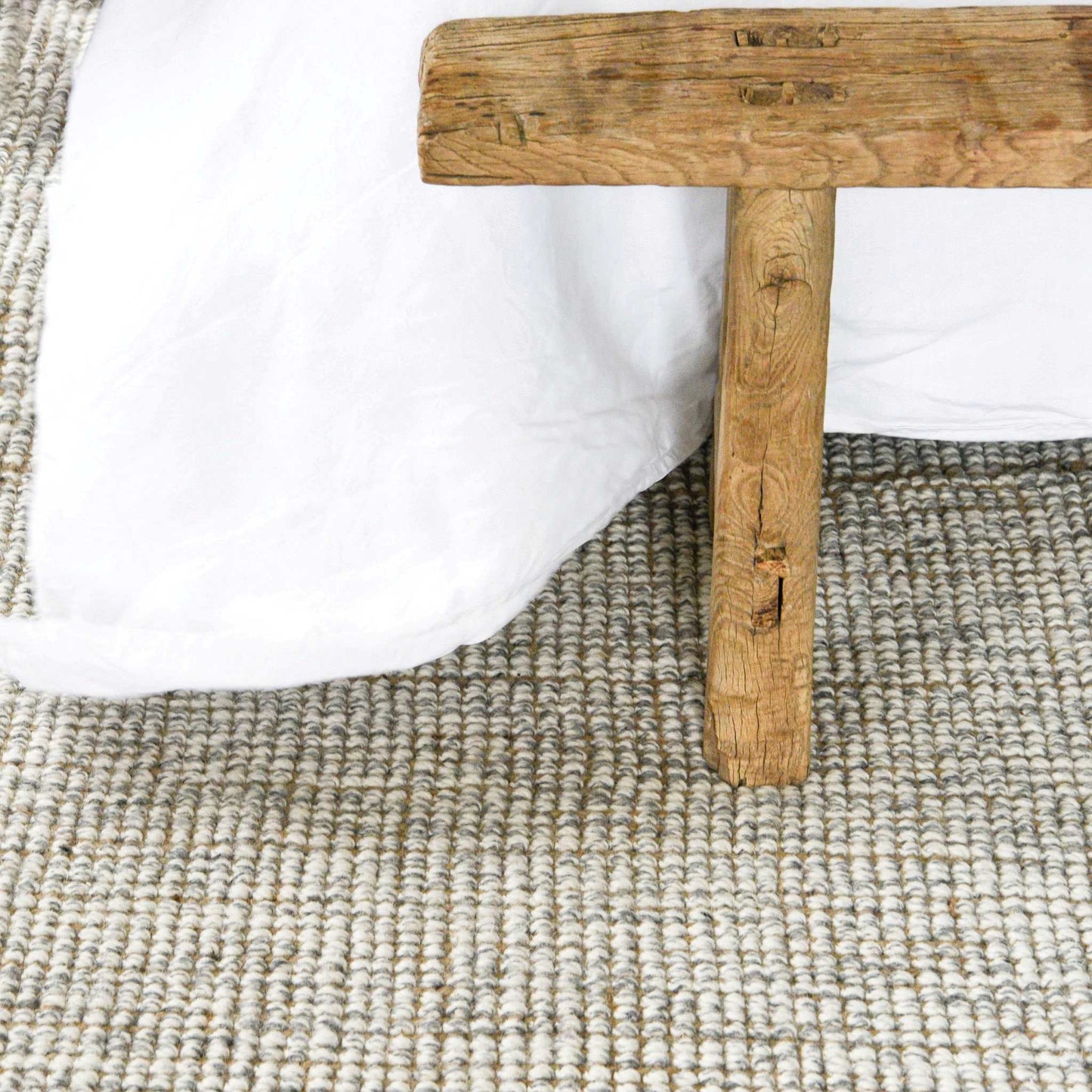 Close up of the carter handcrafted, grey and white heathered wool and jute bouclé rug under a wooden bed frame.