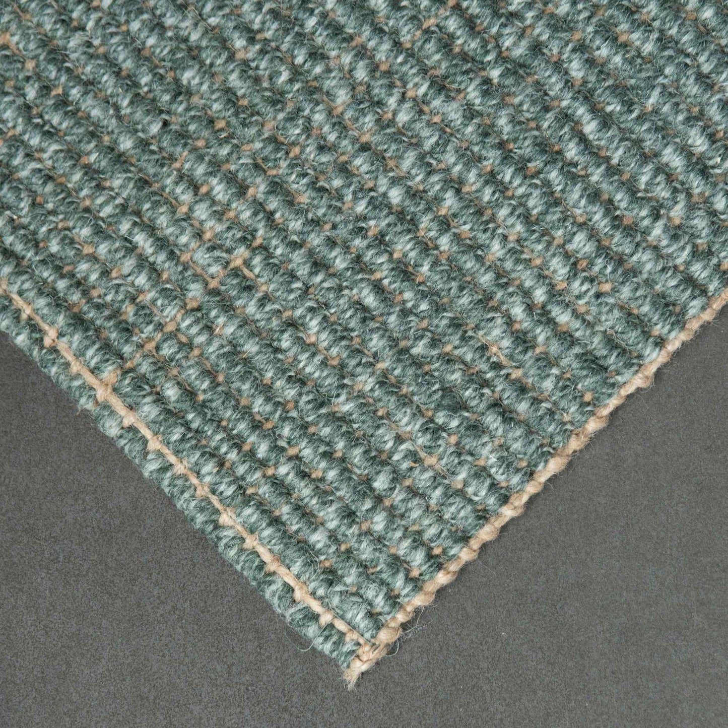 Close-up of Carter Forest handcrafted marled green wool and jute bouclé rug on a slate background.