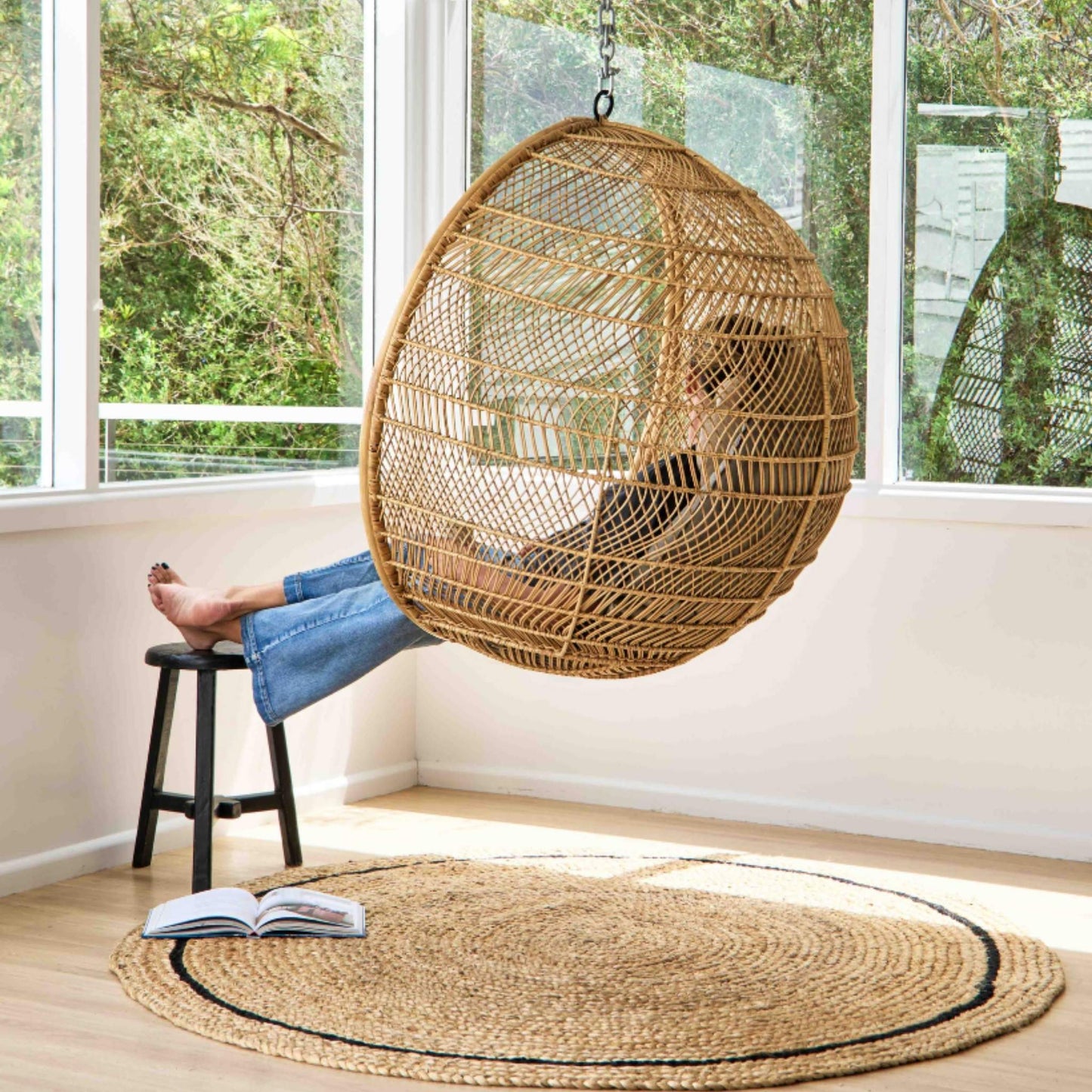 Cooper hand braided jute round rug with a graphite border on a wooden floor in sunlit room.