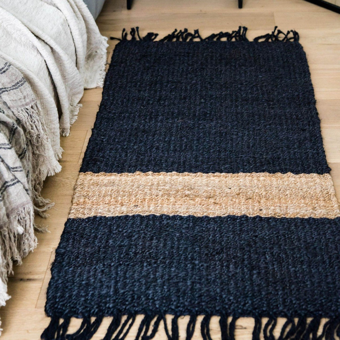 The flat weave texture and graphite stripe on the Irving jute small rug laying next to a bed in a coastal style home.