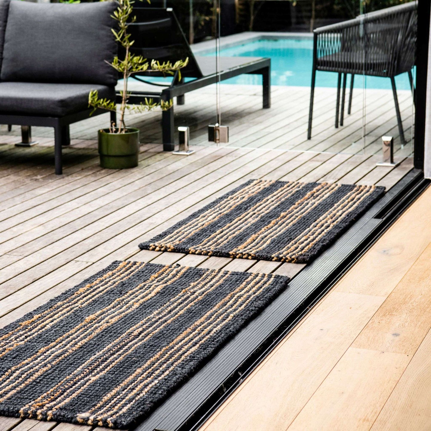 Two handcrafted Jones graphite jute small rugs with natural stripes on wooden deck in pool area.