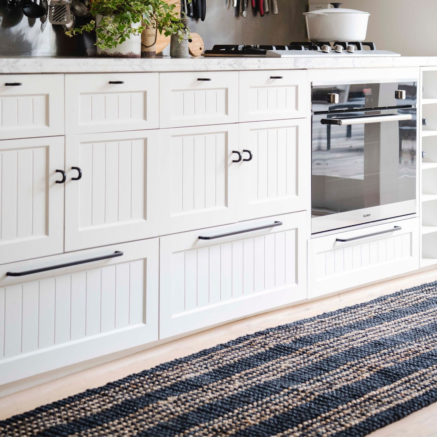 Handcrafted Jones graphite jute small rug with natural stripes on wooden floors in a modern kitchen with white cabinets and black handles.