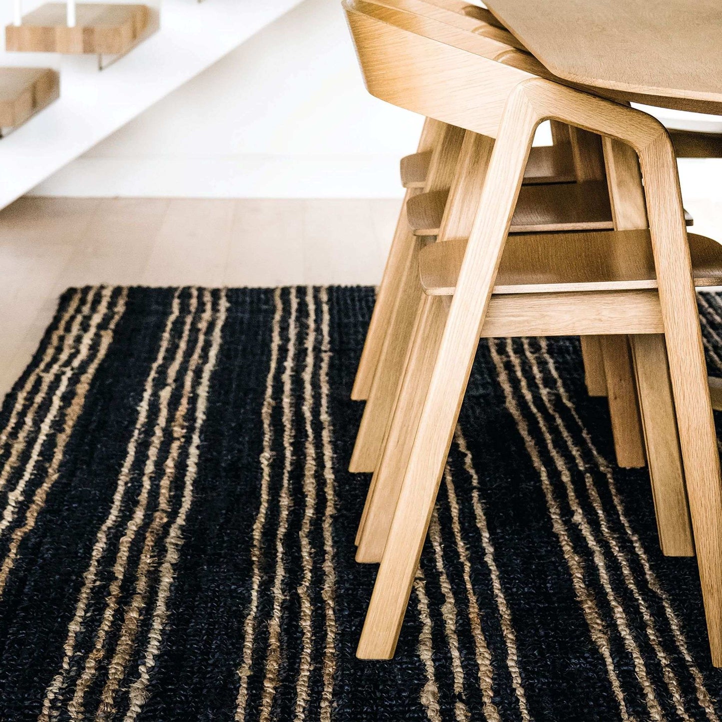Jones graphite boucle textured area rug with a natural stripe under a Scandinavian dining table.