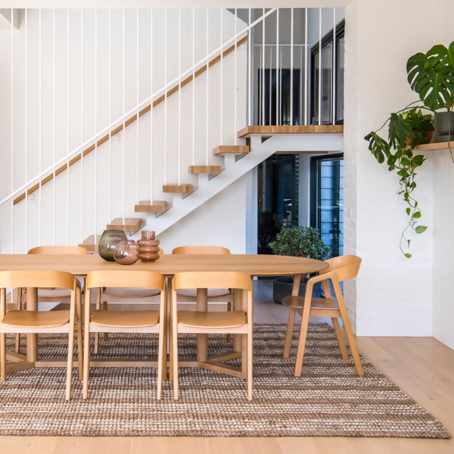Handcrafted Osbourne natural chunky jute bouclé rug with white stripes sitting under a dining table in a Scandinavian style modern room.