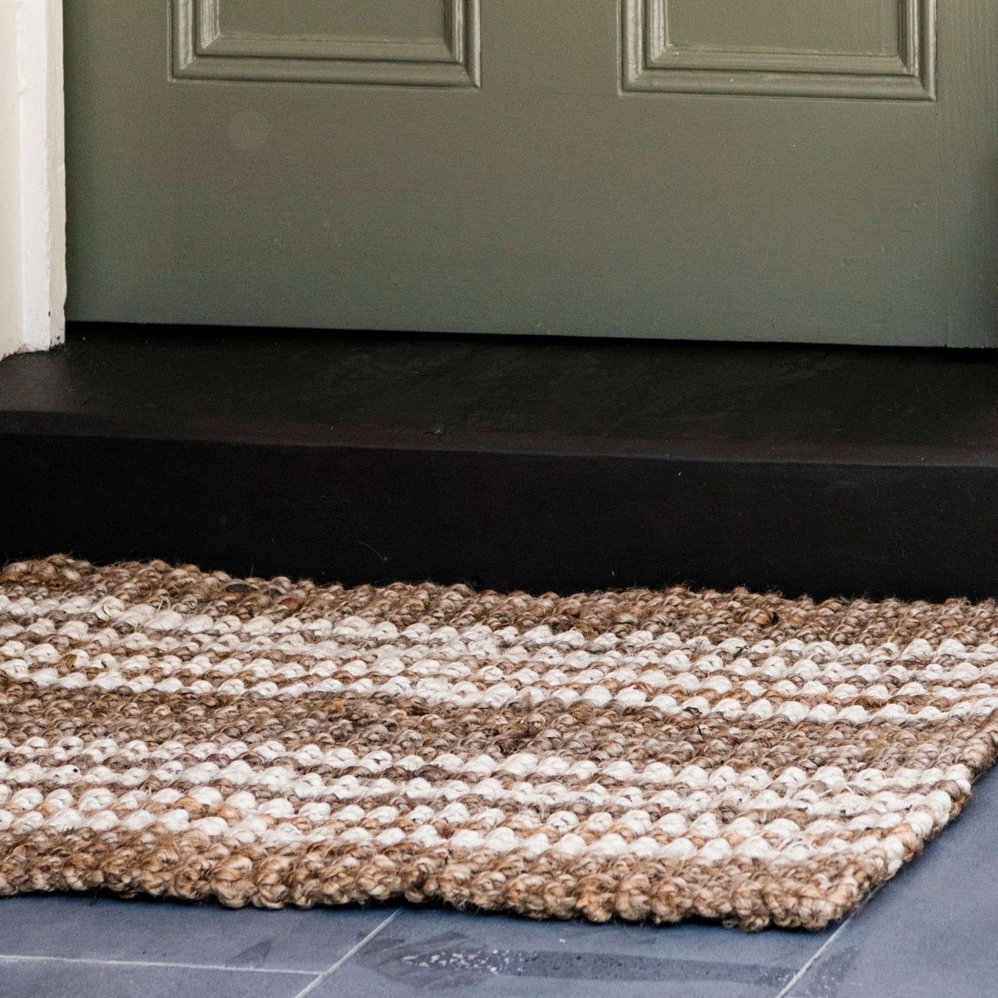 Close-up Osbourne natural chunky jute bouclé rug with white stripes on an undercover front porch.