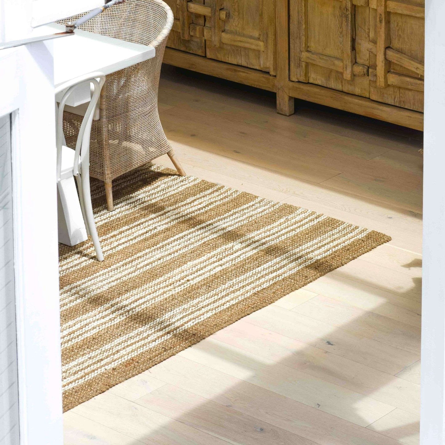 Handcrafted Osbourne natural chunky jute bouclé area rug with white stripes under a dining table in coastal home.