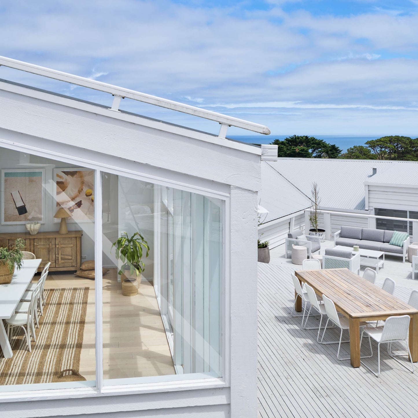 Osbourne natural chunky jute bouclé area rug with white stripes under a dining table with a view of a modern rooftop terrace and ocean view.