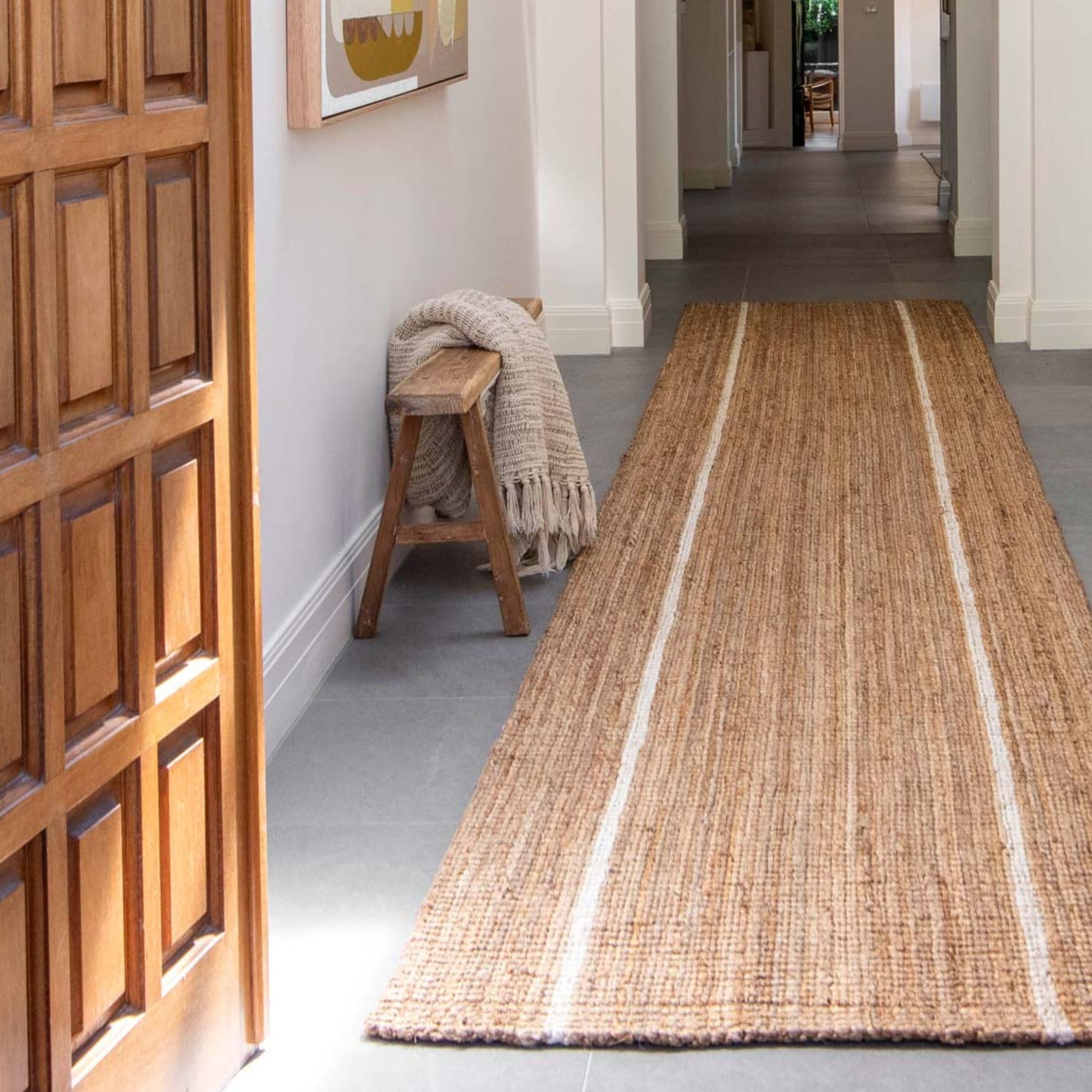 Robinson runner rug in natural bouclé jute with two white stripes in an entryway on polished concrete floors.