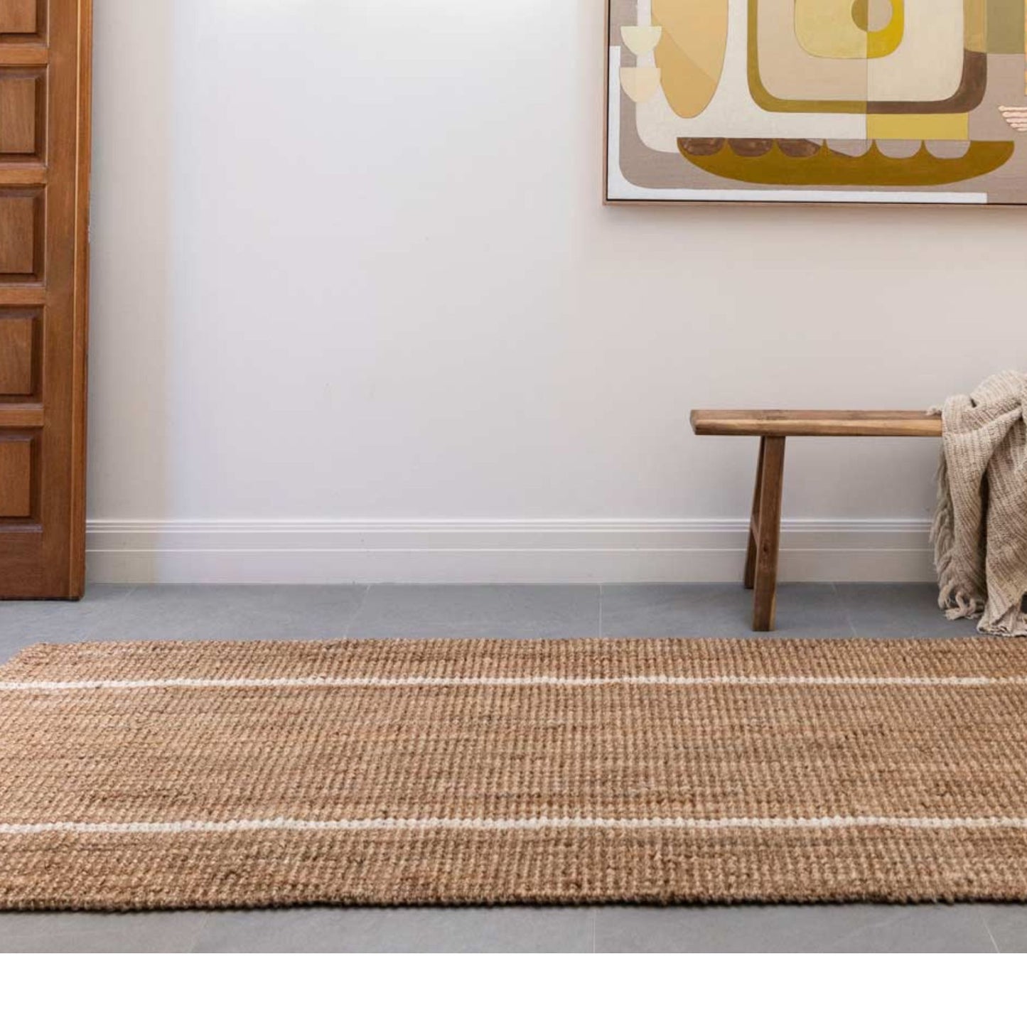 Robinson runner rug in natural bouclé jute with two white stripes in an entryway on polished concrete floors.