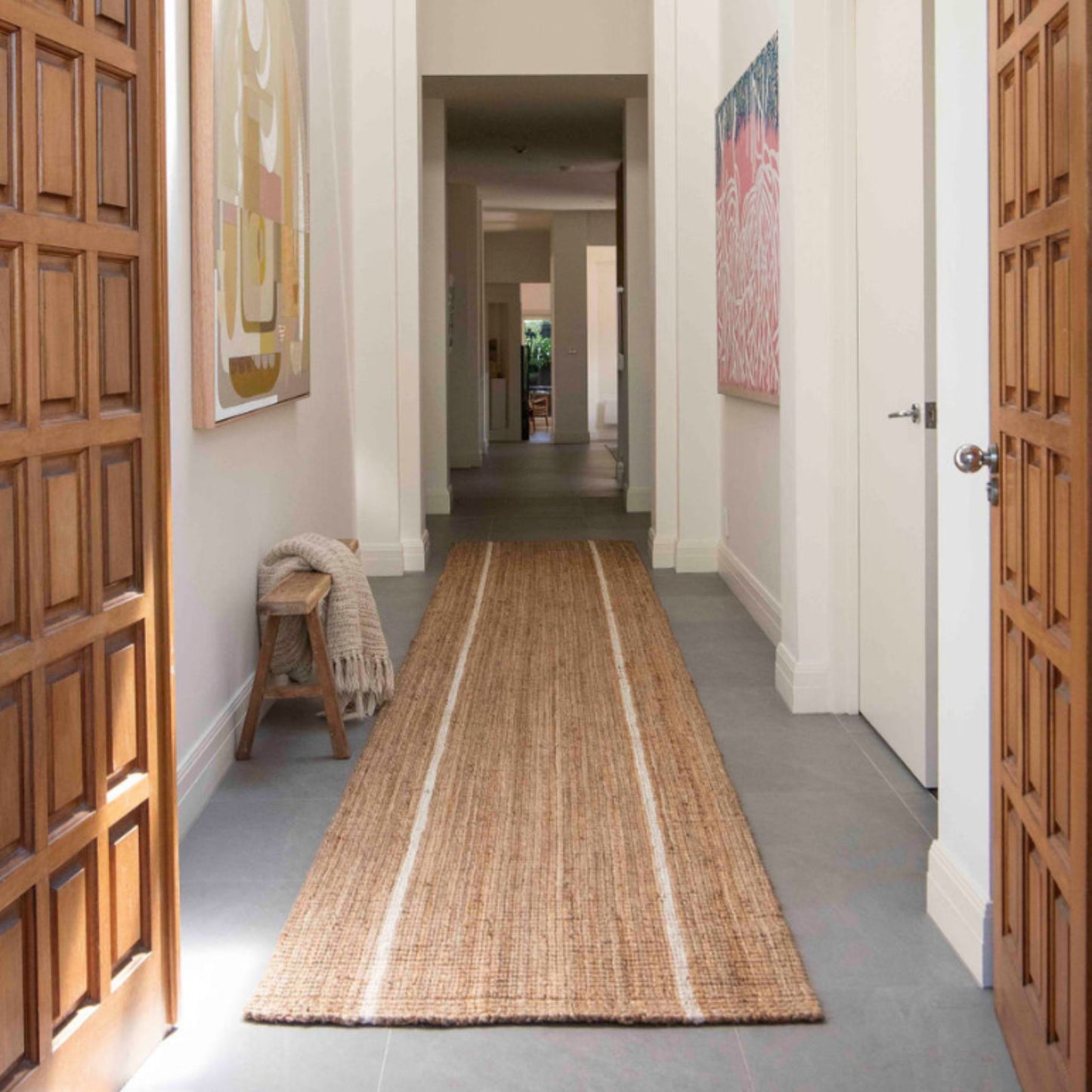 Robinson large runner rug in natural bouclé jute with two white stripes in an entryway on polished concrete floors in a modern home.