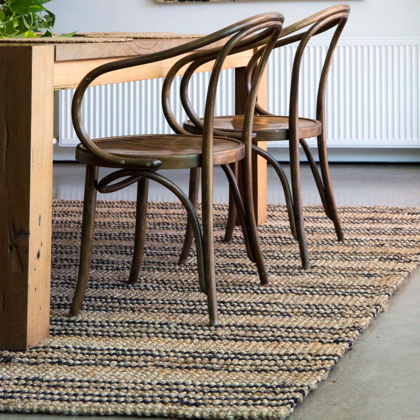 Smith jute natural bouclé area rug with graphite stripes on polished concrete floors under a dining table and modern casual chairs.