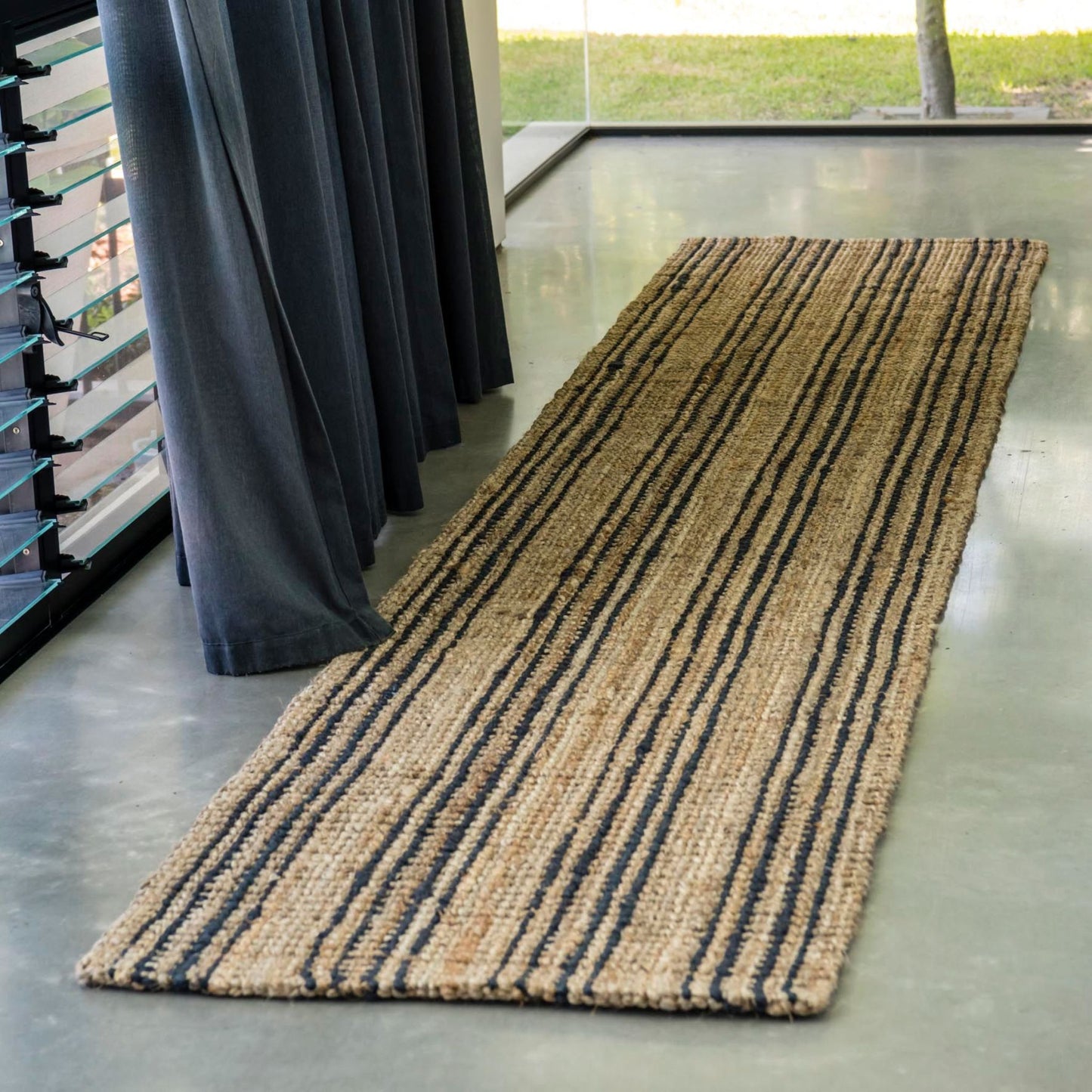 Smith natural bouclé jute runner rug with graphite stripes on polished concrete floor entryway in a modern house.