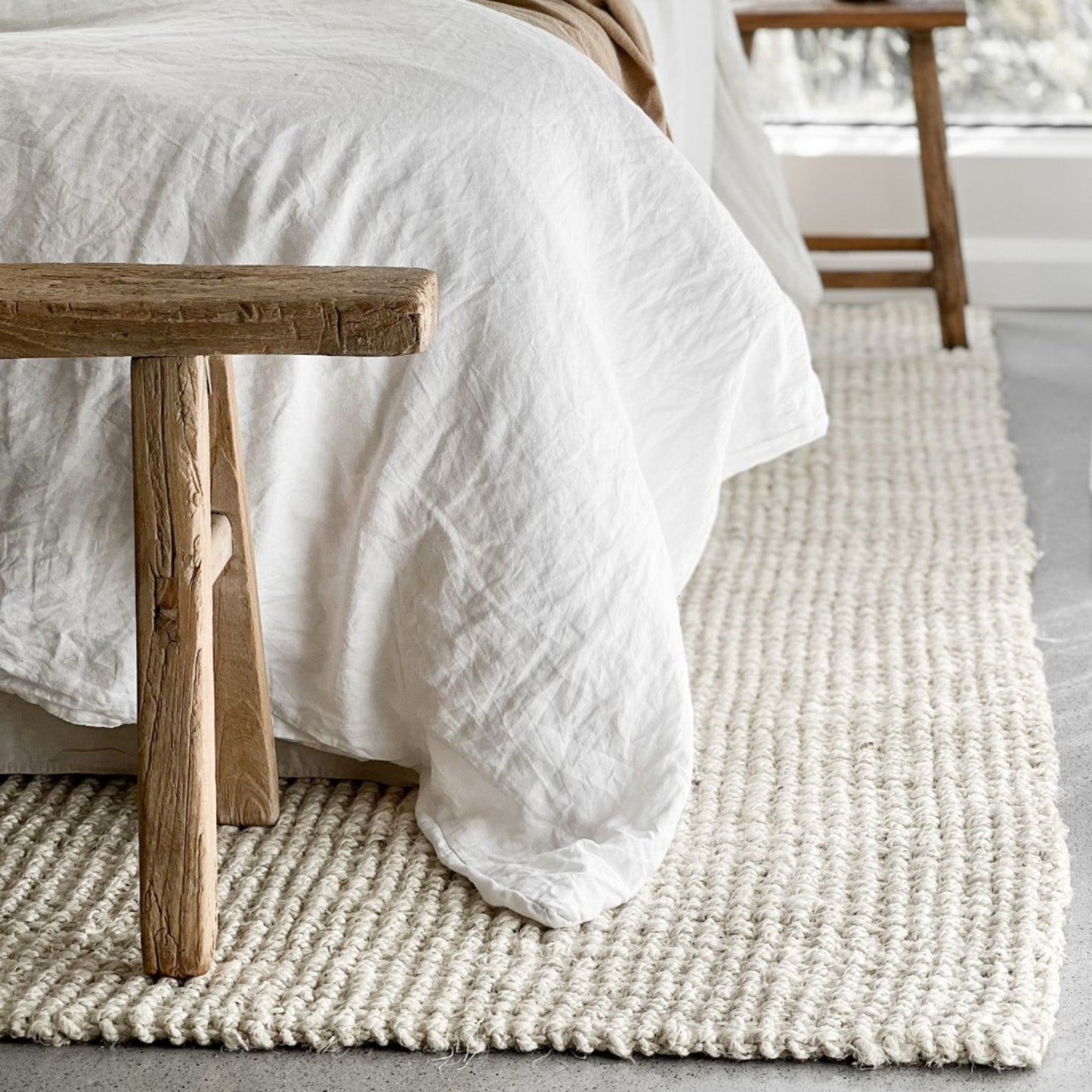 Vincent, whitewashed jute bouclé rug on polished concrete in a coastal style bedroom with white and timber furnishings.