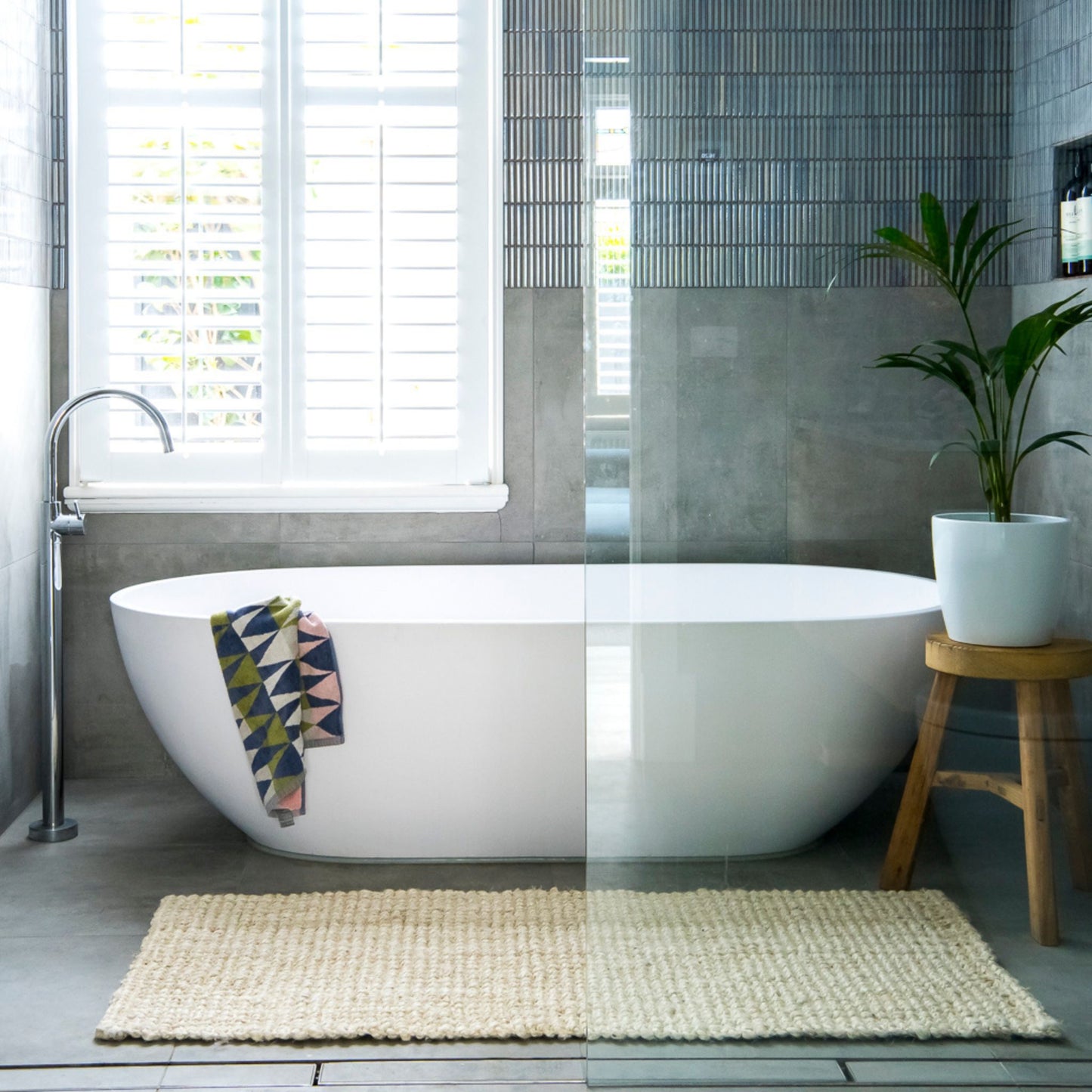 Vincent, whitewashed, chunky jute bouclé small rug on polished concrete in a coastal style bathroom with a white tub and timber stool.