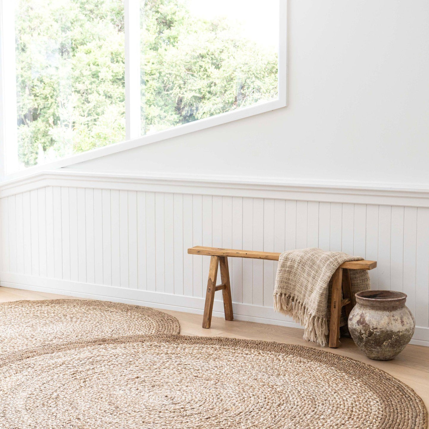 Westmore hand-braided two toned jute round rug with a border sitting on a light wooden floor in a sunlit, coastal style home.
