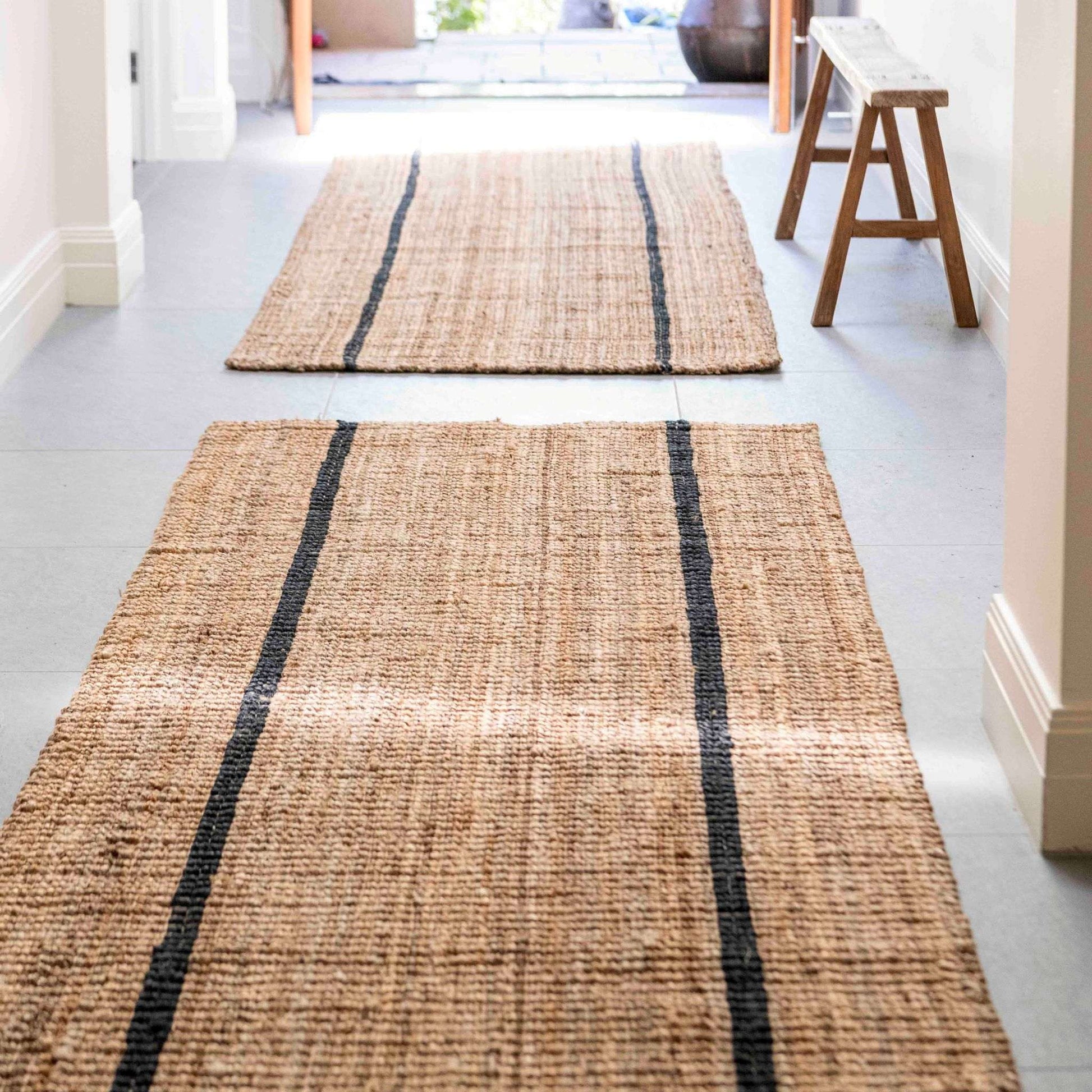 Handcrafted bailey stripe chunky jute bouclé runners rug in a modern  entryway with brushed concrete floors and wooden bench. 