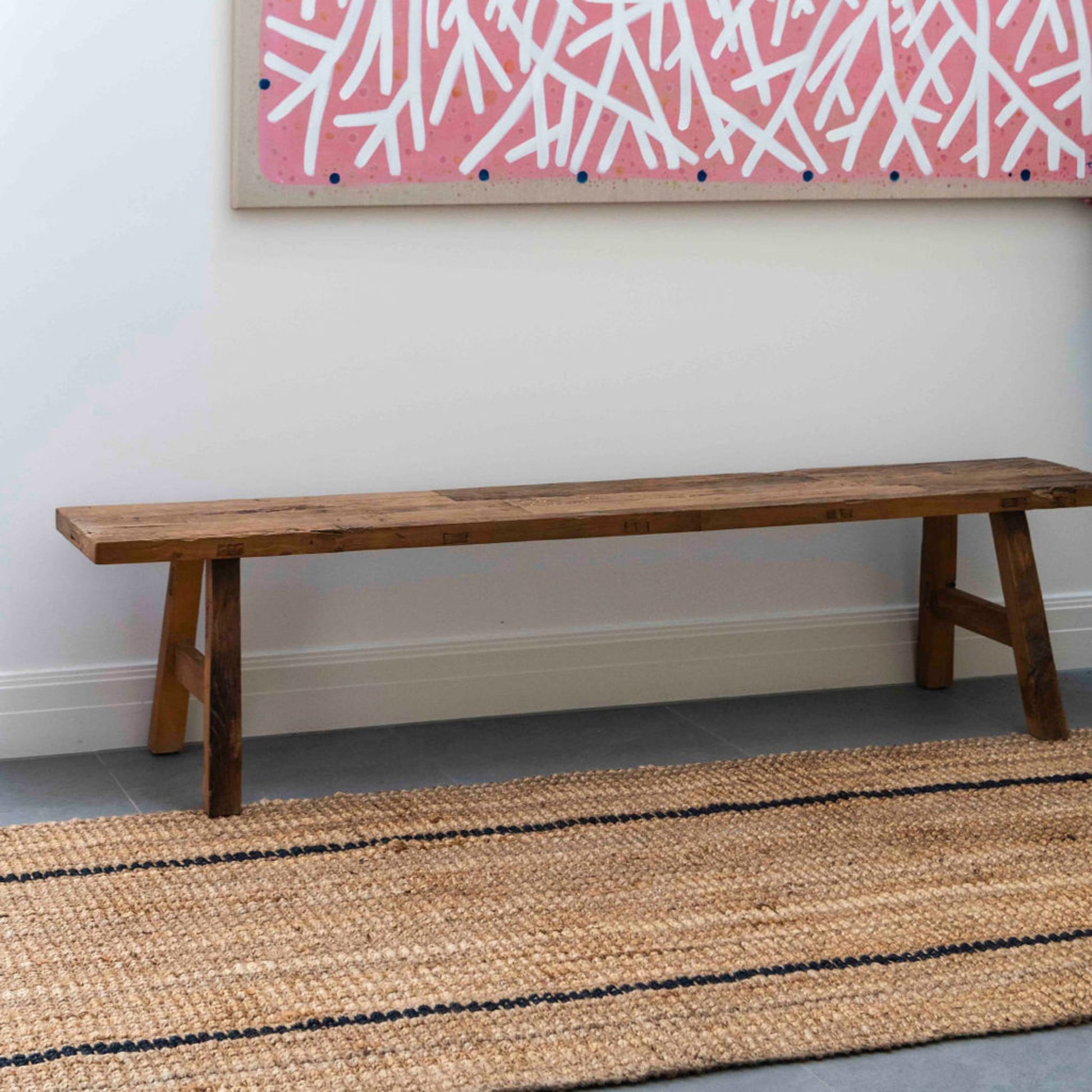 Handcrafted bailey stripe chunky jute bouclé runner rug in a modern entryway with brushed concrete floors and wooden bench. 