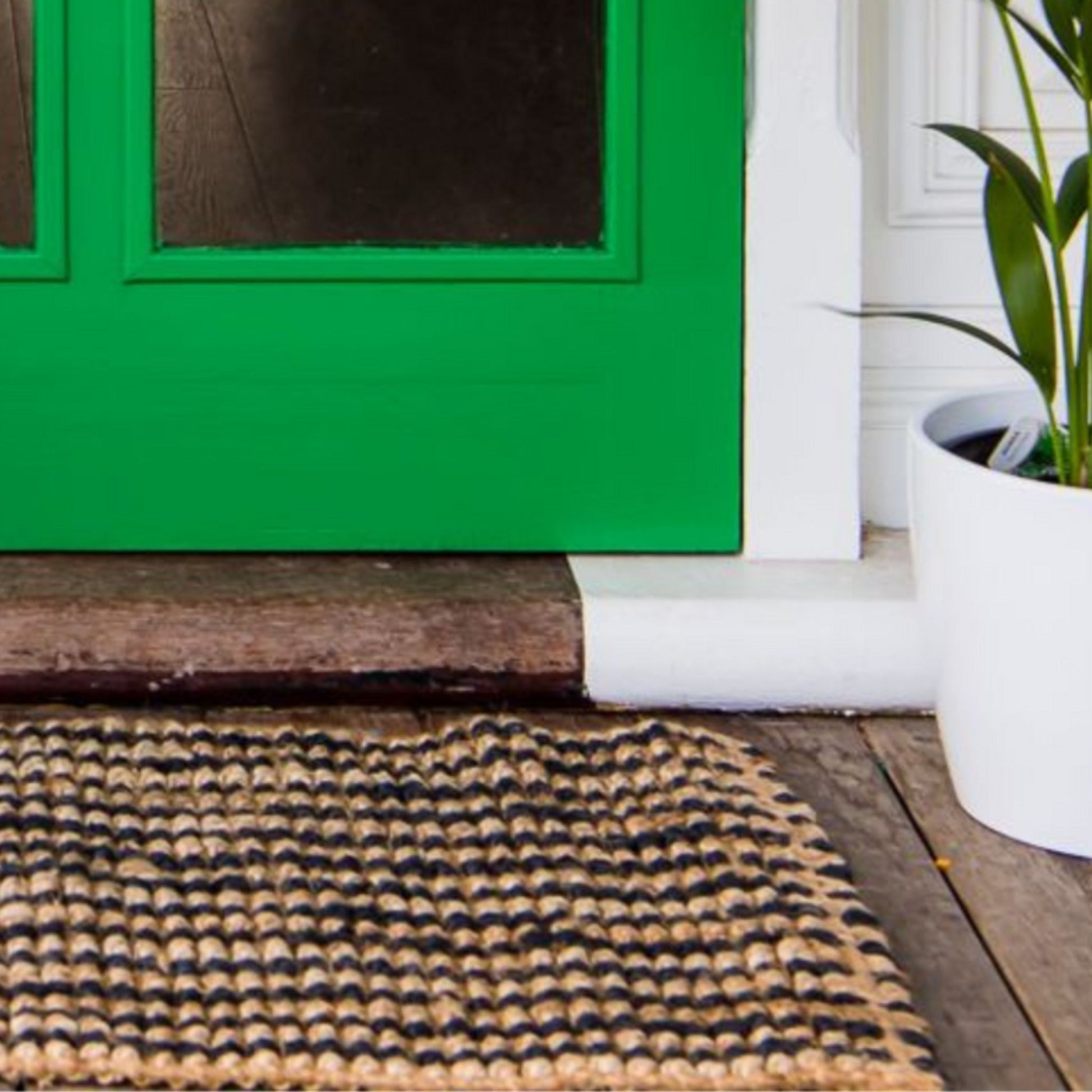 Handcrafted striped Caravan striped jute rug in a small size, placed at a green front door on wooden decking.