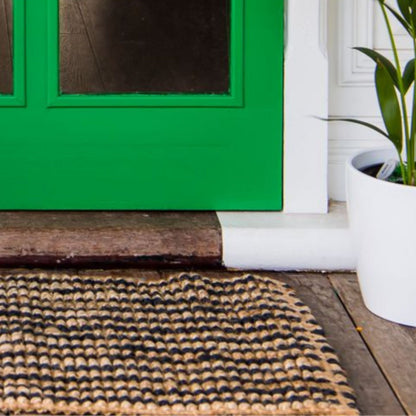Handcrafted striped Caravan striped jute rug in a small size, placed at a green front door on wooden decking.