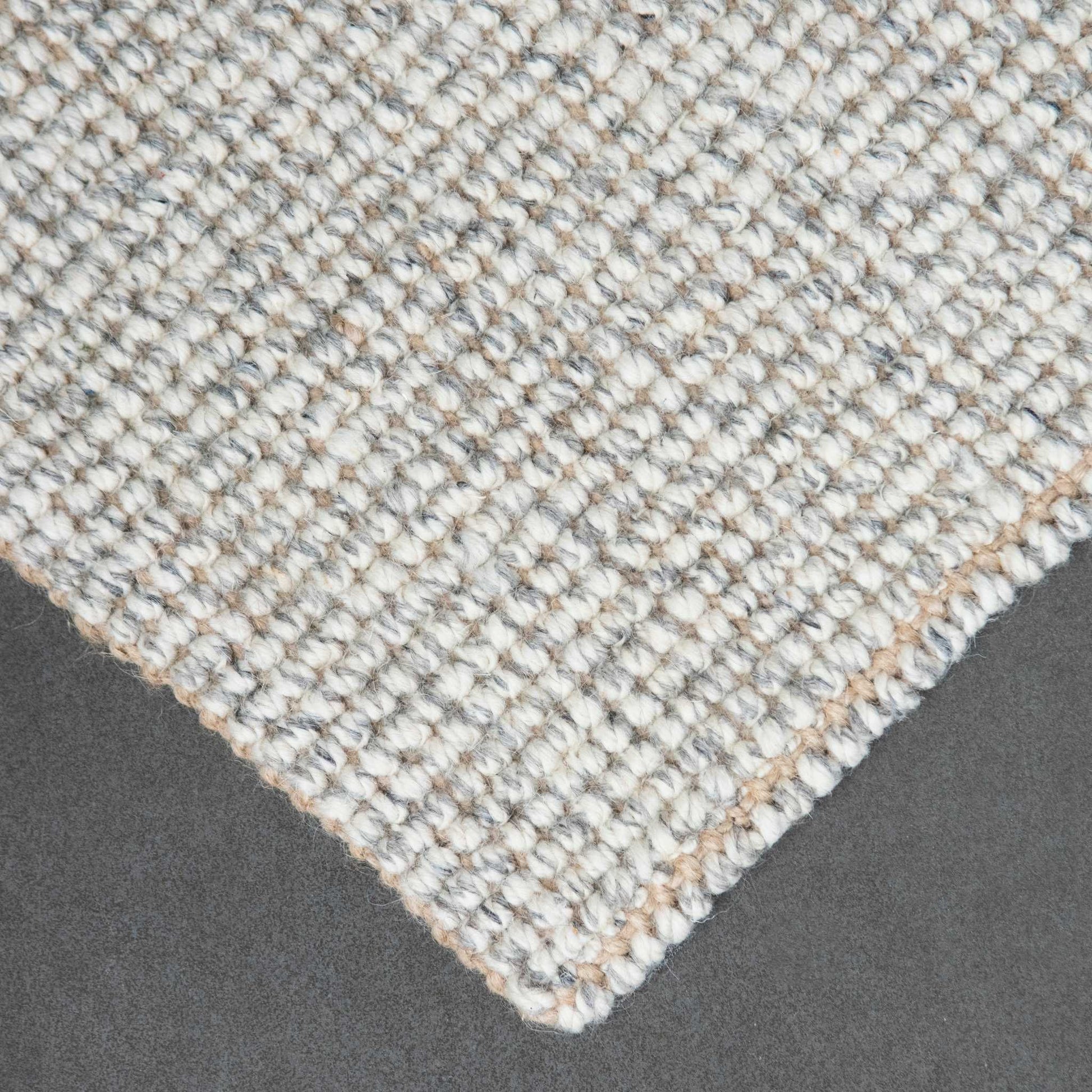 Close-up of Carter handcrafted  grey white heathered wool and jute bouclé rug on slate background.