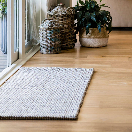 Carter handcrafted, grey and white heathered wool and jute bouclé rug on a wooden floor entryway. 