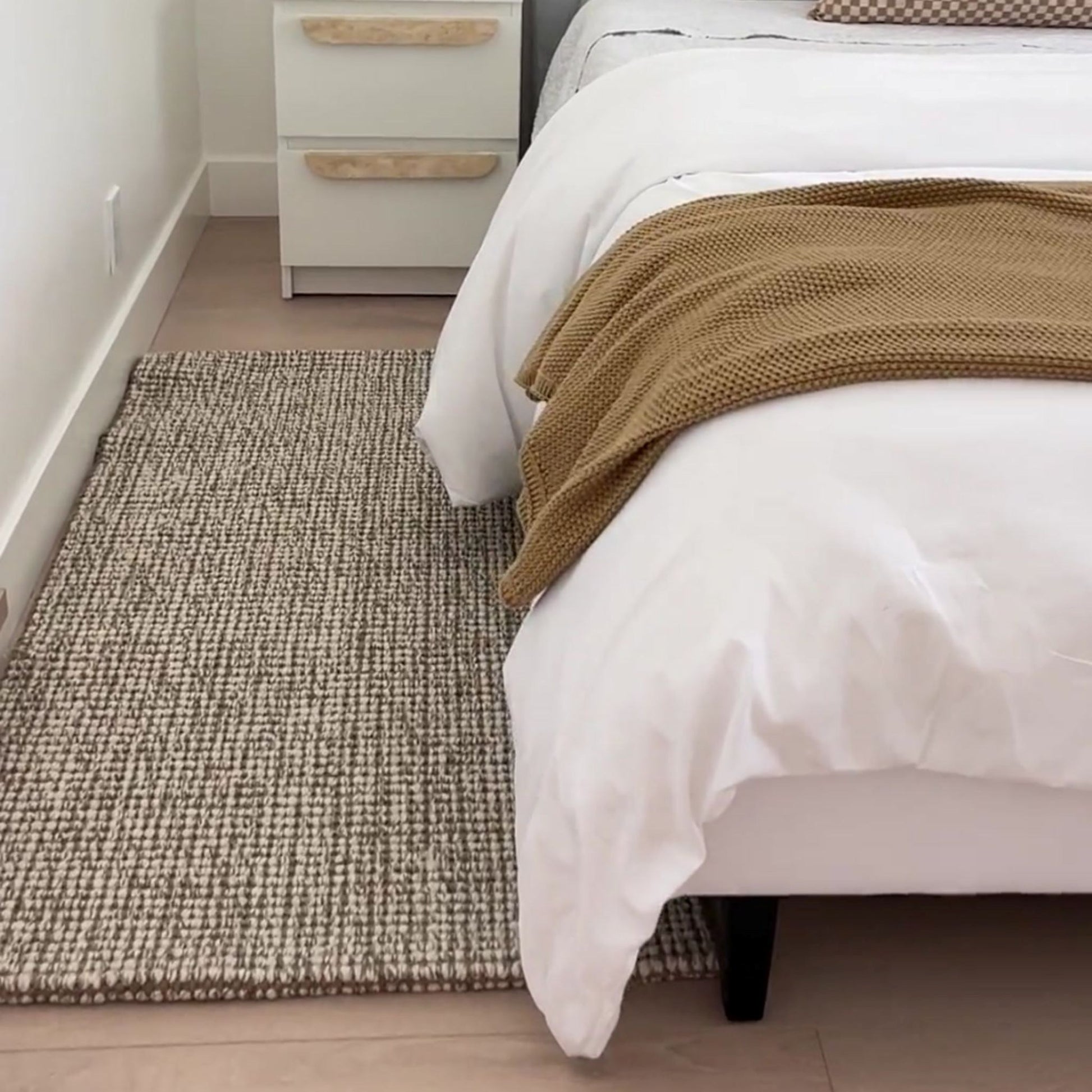 Carter handcrafted, grey and white heathered wool and jute bouclé small rug on a wooden floor next to a bed.