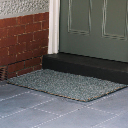 Carter forest small rug in marled green wool and jute bouclé rug sitting on on slate tile at an undercover entrance. 