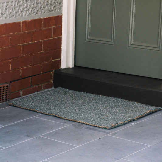 Carter forest small rug in marled green wool and jute bouclé rug sitting on on slate tile at an undercover entrance. 