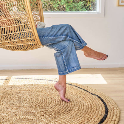 Cooper hand braided soft, jute, round rug with a graphite border on a wooden floor in sunlit room.