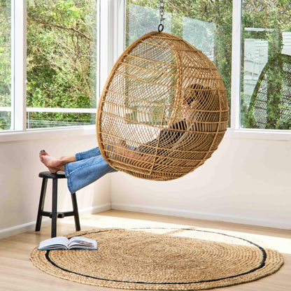 Cooper hand braided jute round rug with a graphite border on a wooden floor in sunlit room.  