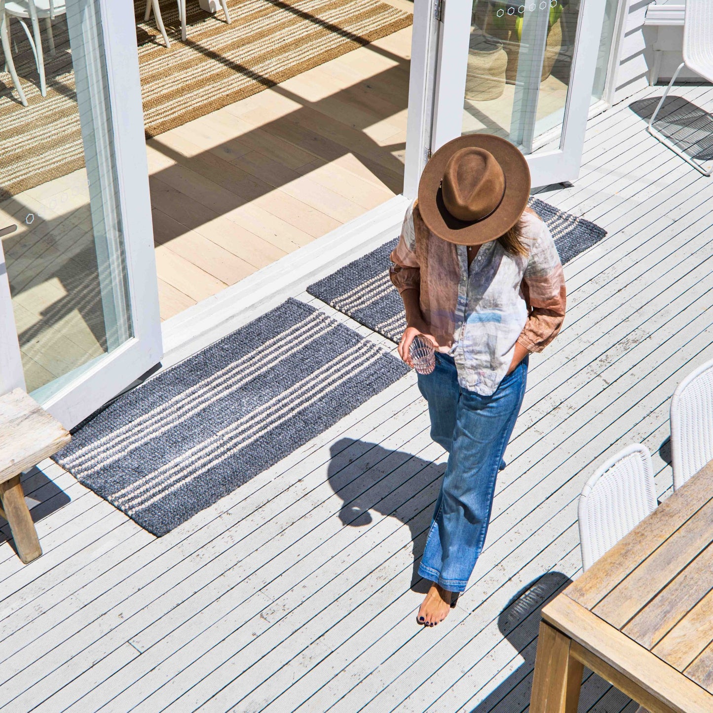 Macintosh flatweave slate grey rug with natural stripes, made from 100% recycled PET sitting at entryway on white washed, timber deck.