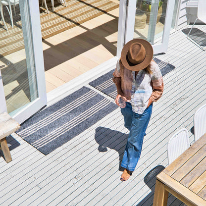 Macintosh flatweave slate grey rug with natural stripes, made from 100% recycled PET sitting at entryway on white washed, timber deck.