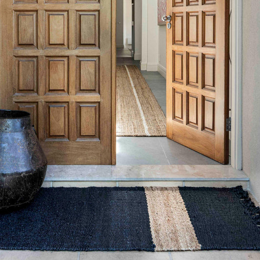 Handcrafted Irving stripe jute flatweave rug on polished concrete floor at an entrance to a home. 