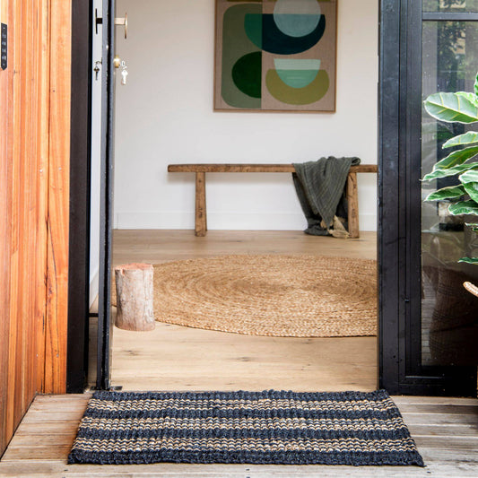 Handcrafted Jones graphite jute small rug with natural stripes on wooden deck at door entrance. 