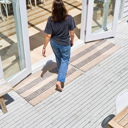 Macintosh flatweave rug, with natural and slate grey stripes made from 100% recycled PET sitting on white, timber outdoor deck.  