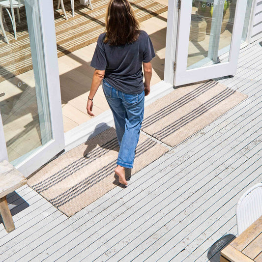 Macintosh flatweave rug, with natural and slate grey stripes made from 100% recycled PET sitting on white, timber outdoor deck.  