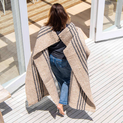 Macintosh flatweave rug, with natural and slate grey stripes made from 100% recycled PET, being carried and showing soft, light texture.