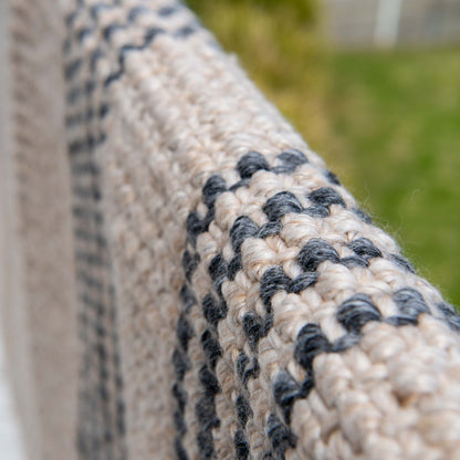 Close-up of Macintosh flatweave rug, with natural and slate grey stripes made from 100% recycled PET hanging on coastal balcony.