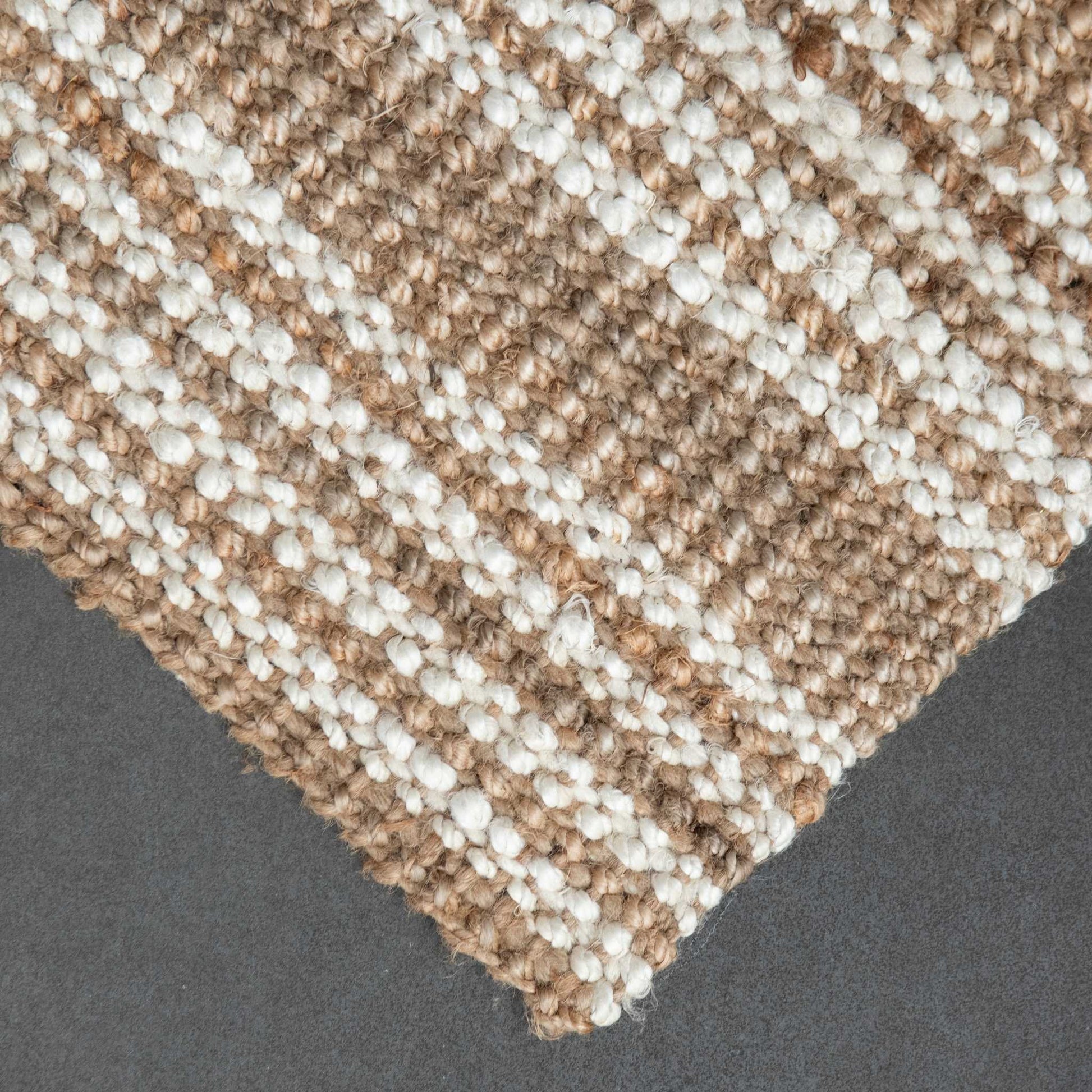 Close-up of Osbourne natural and white striped jute rug with a chunky, bouclé weave on slate  background.