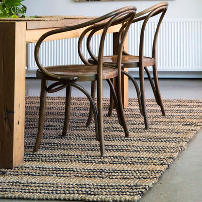 Smith jute natural bouclé area rug with graphite stripes on polished concrete floors under a dining table and modern casual chairs. 