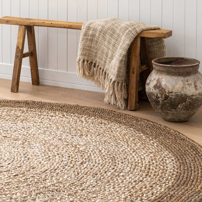 Westmore hand-braided two toned jute round rug with a border sitting on a light wooden floor in a sunlit, coastal style home.