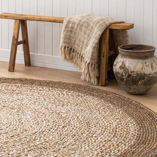 Westmore hand-braided two toned jute round rug with a border sitting on a light wooden floor in a sunlit, coastal style home.